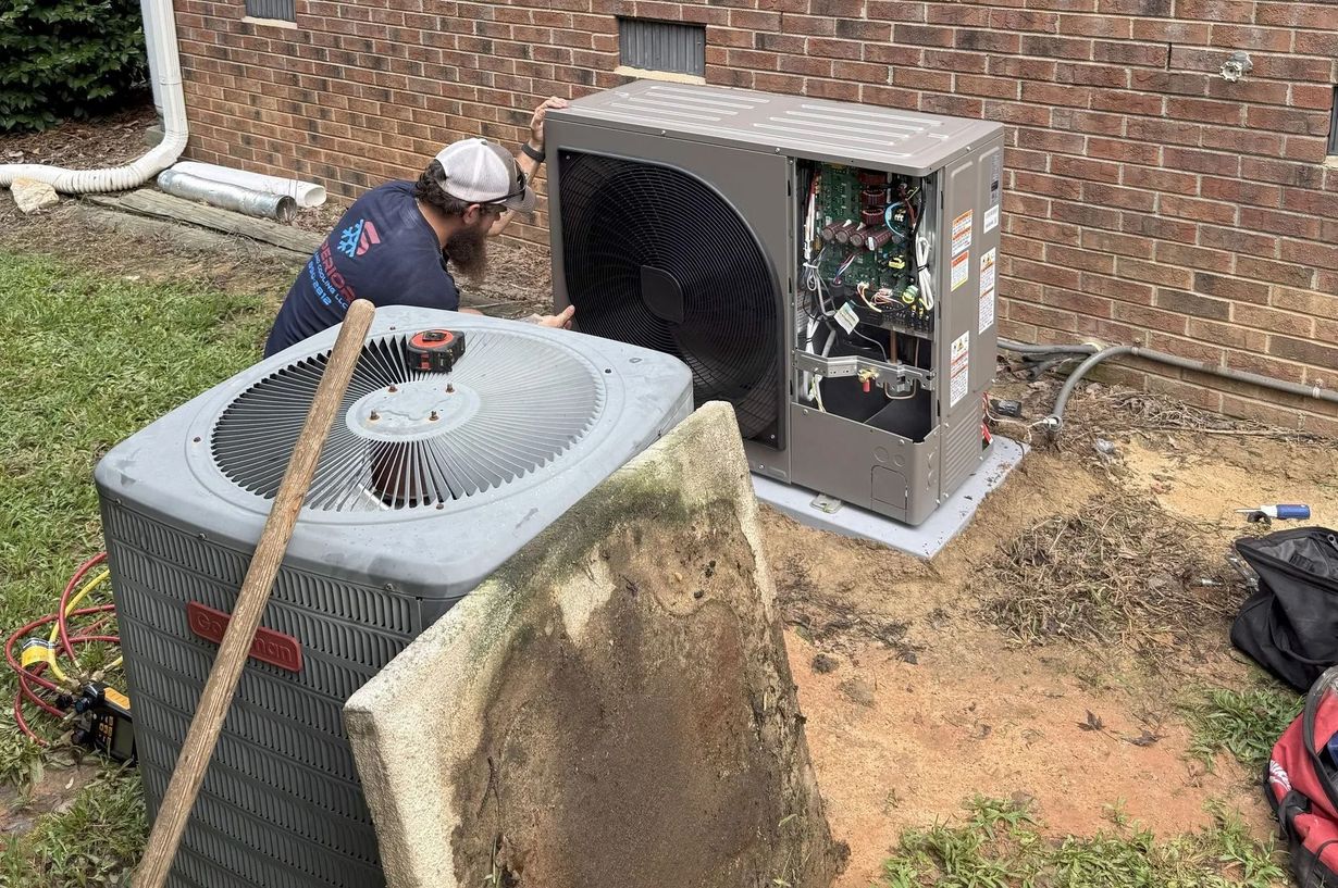 HVAC technician working on outdoor air conditioning units near a brick wall.