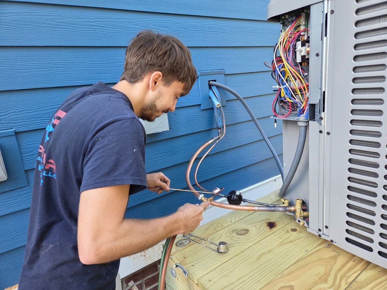 HVAC technician working on an air conditioning unit outside a blue-sided building.