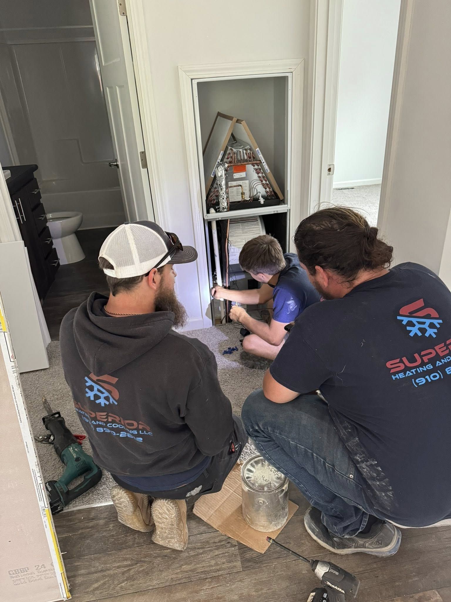 Three people working on equipment in a closet. One uses a flashlight. Gray walls, light wood floors.