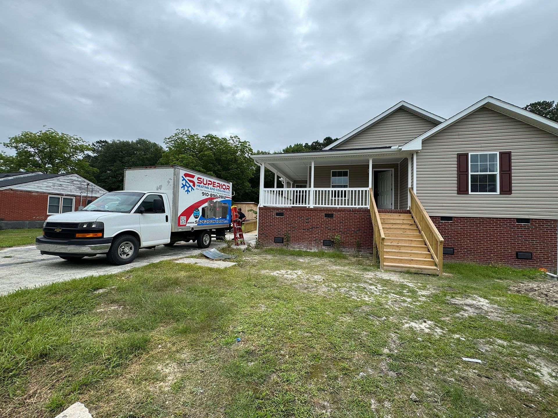 A moving truck parked near a house with a porch and new stairs, gravel driveway, and overcast sky.