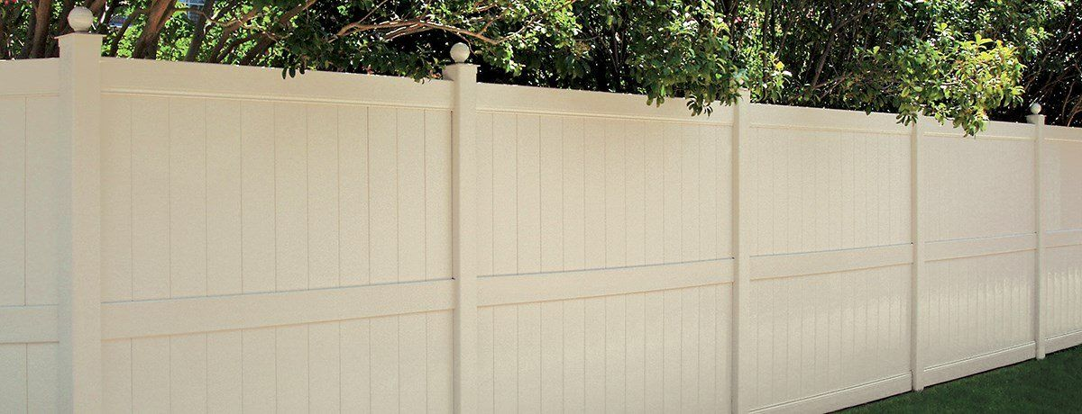 A white vinyl fence is surrounded by trees in a backyard.