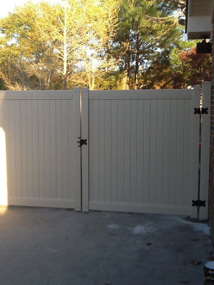 A white fence with black hinges is in a driveway.