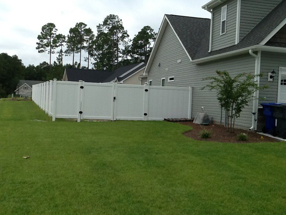 A white fence surrounds a lush green yard in front of a house