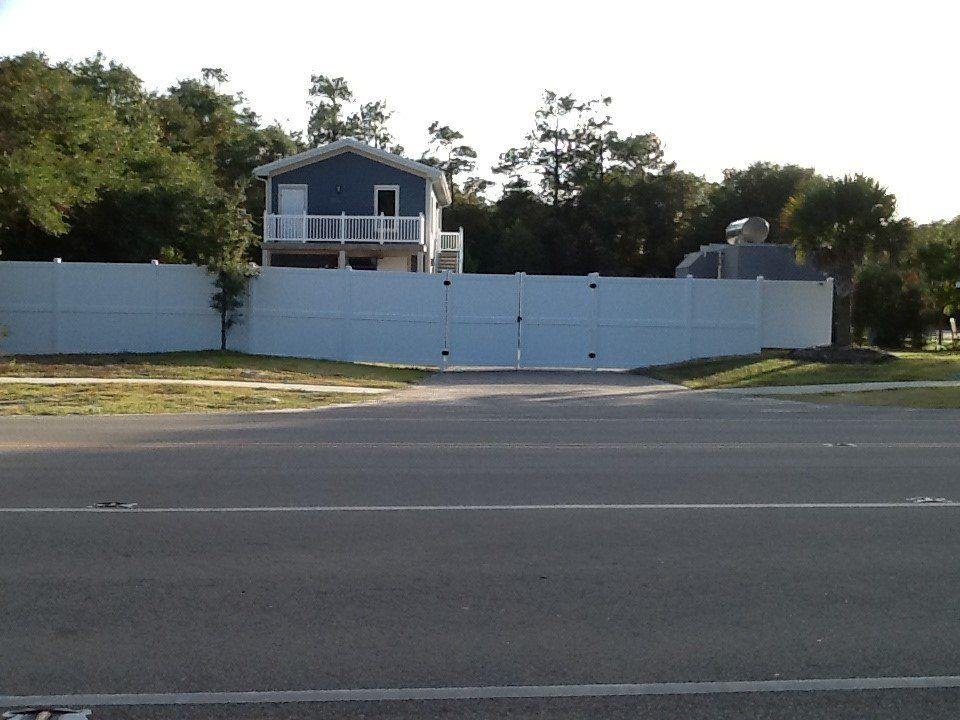 A white fence surrounds a house on the side of the road