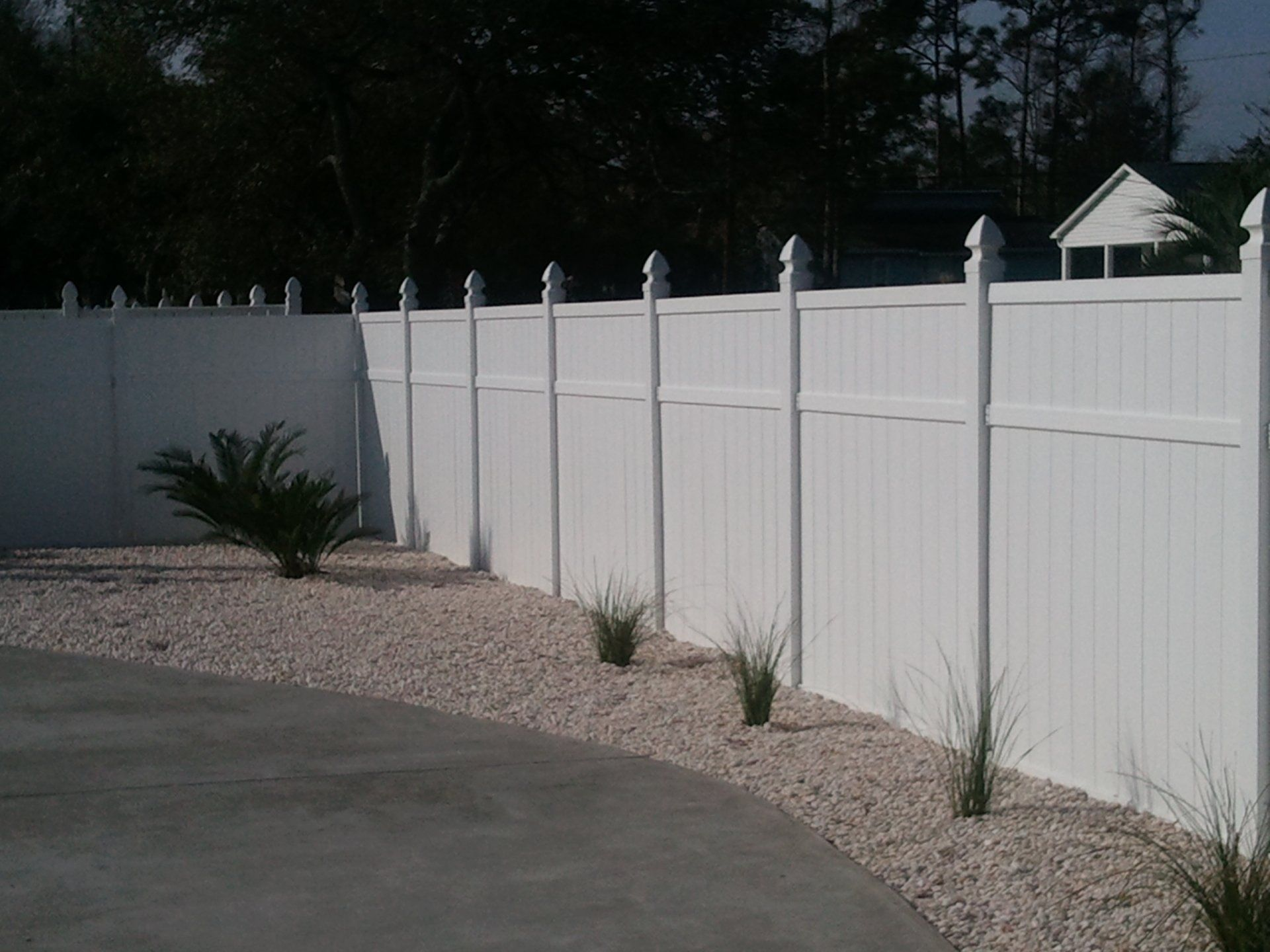 A white fence is surrounded by gravel and plants