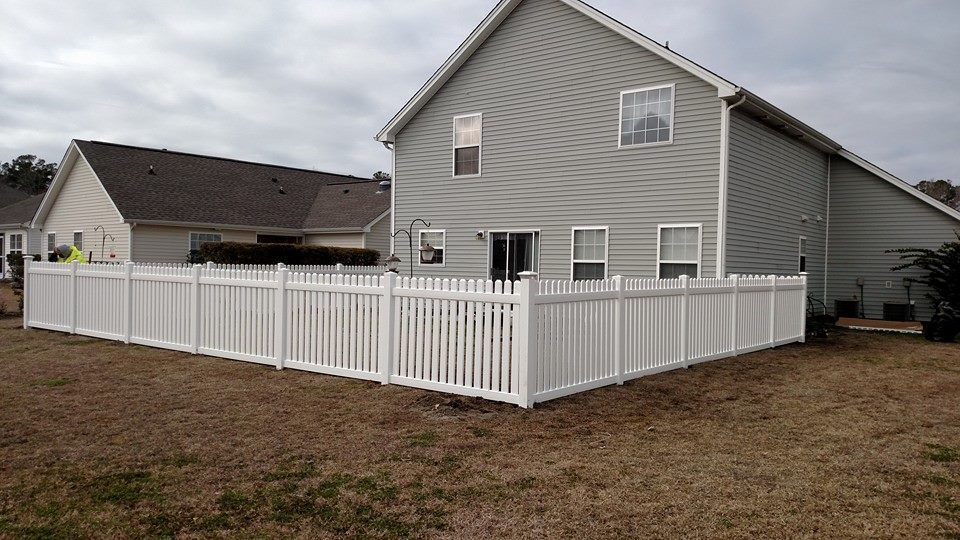 A white fence surrounds the backyard of a house.