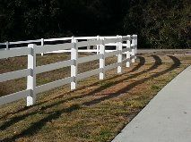 A white fence surrounds a grassy field next to a sidewalk.