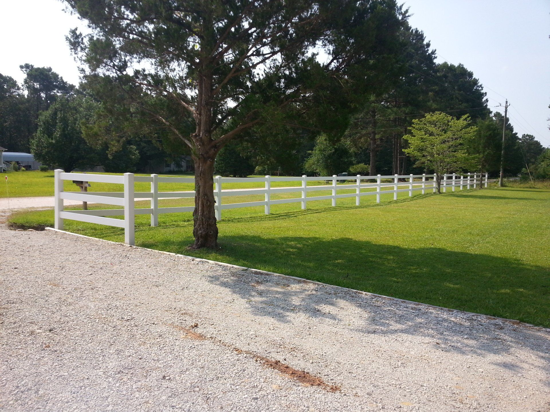 A white fence surrounds a grassy field with trees in the background
