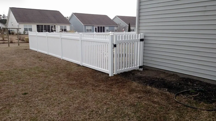 A white fence is sitting next to a house in a backyard.