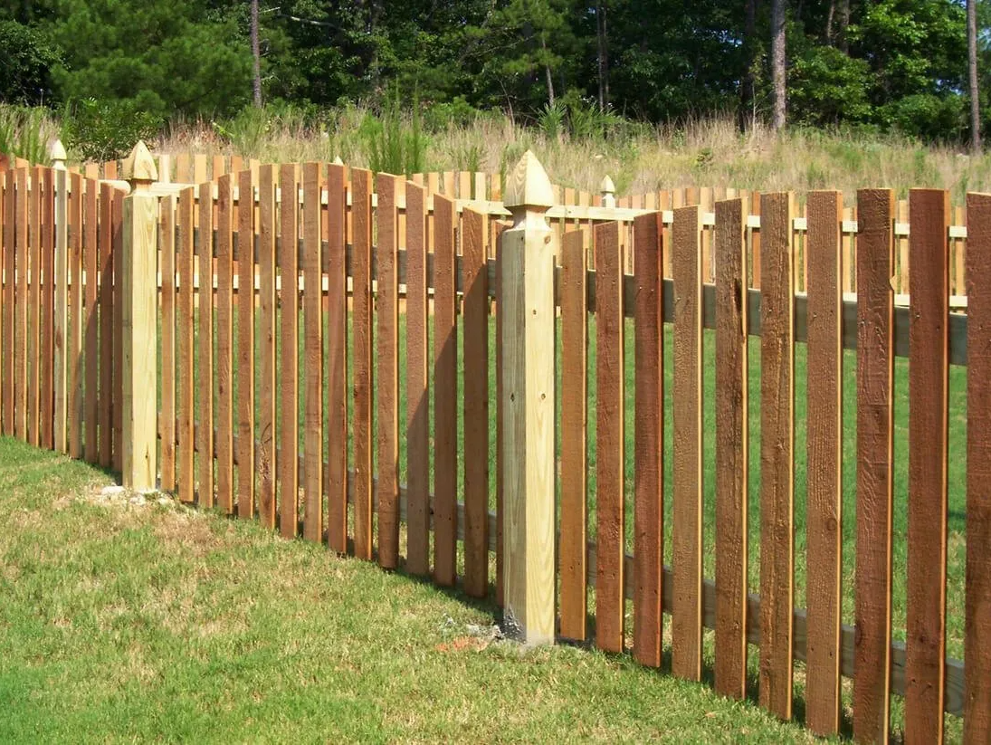 A wooden picket fence is sitting on top of a lush green field.