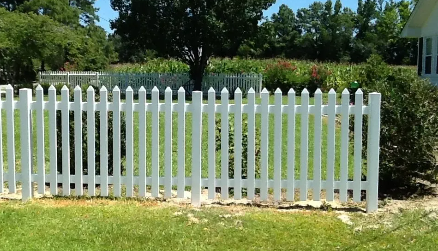 A white picket fence surrounds a grassy yard in front of a house.