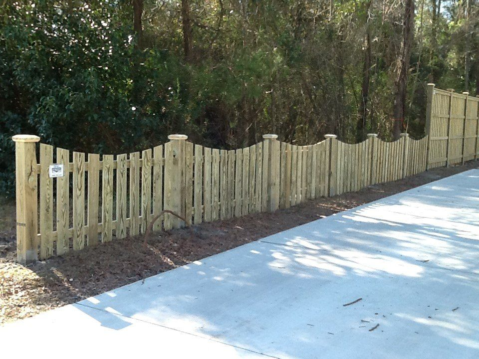 A wooden fence along a concrete driveway with trees in the background