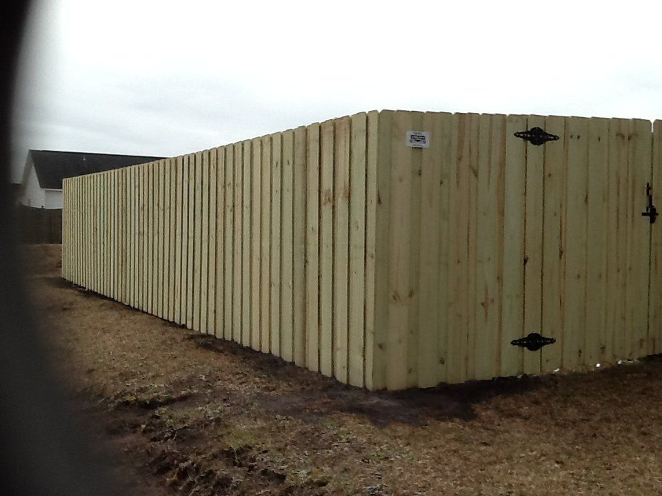 A long wooden fence with a black door and a house in the background.
