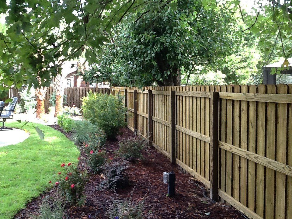 A wooden fence surrounds a garden with a bench in the background.