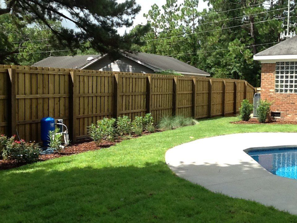 A wooden fence surrounds a swimming pool in a backyard