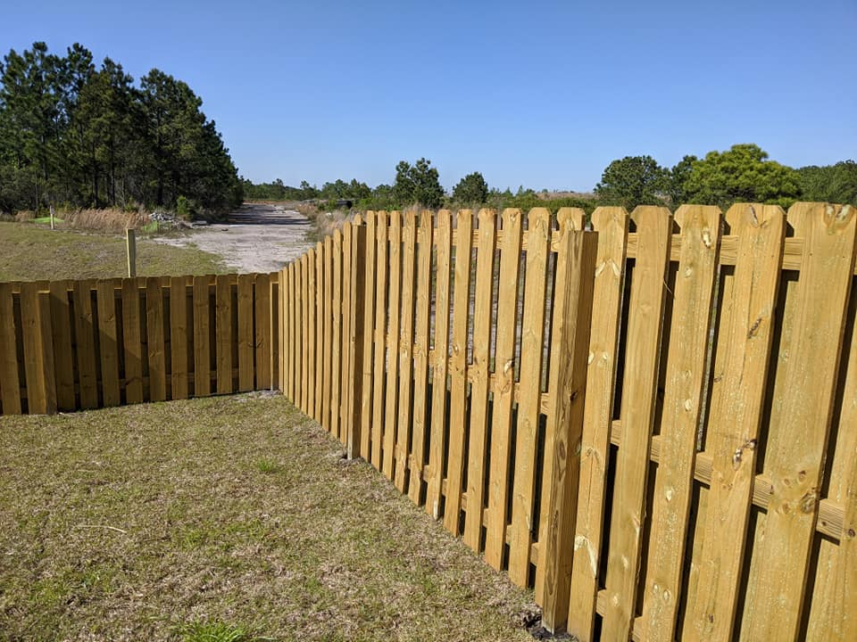 A wooden fence surrounds a grassy field with trees in the background
