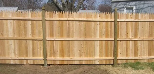 A wooden fence is sitting on top of a dirt field next to a house.