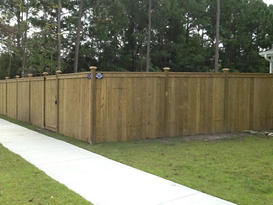 A wooden fence along a sidewalk with trees in the background