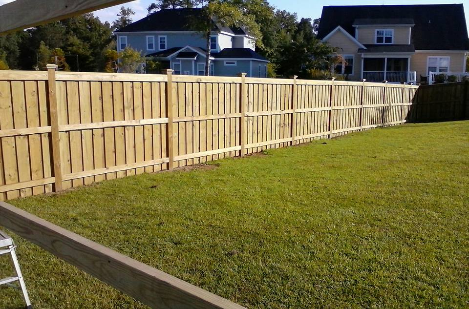 A wooden fence surrounds a lush green yard in front of a house