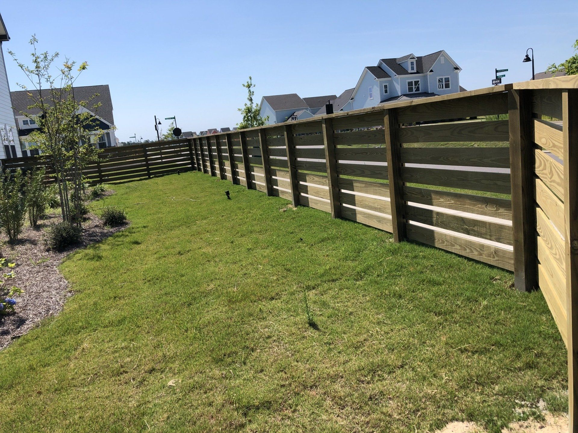 A wooden fence surrounds a lush green field with houses in the background.