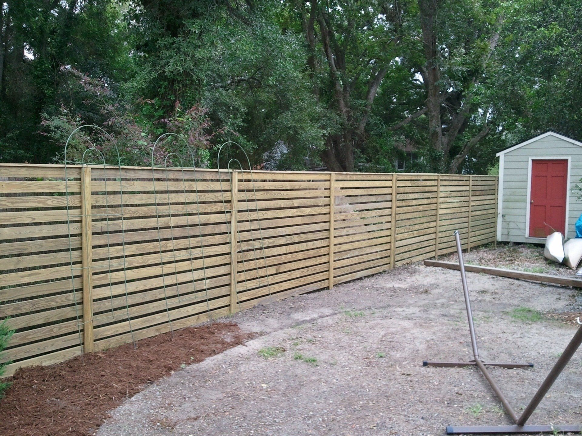 A wooden fence in a backyard with a shed in the background