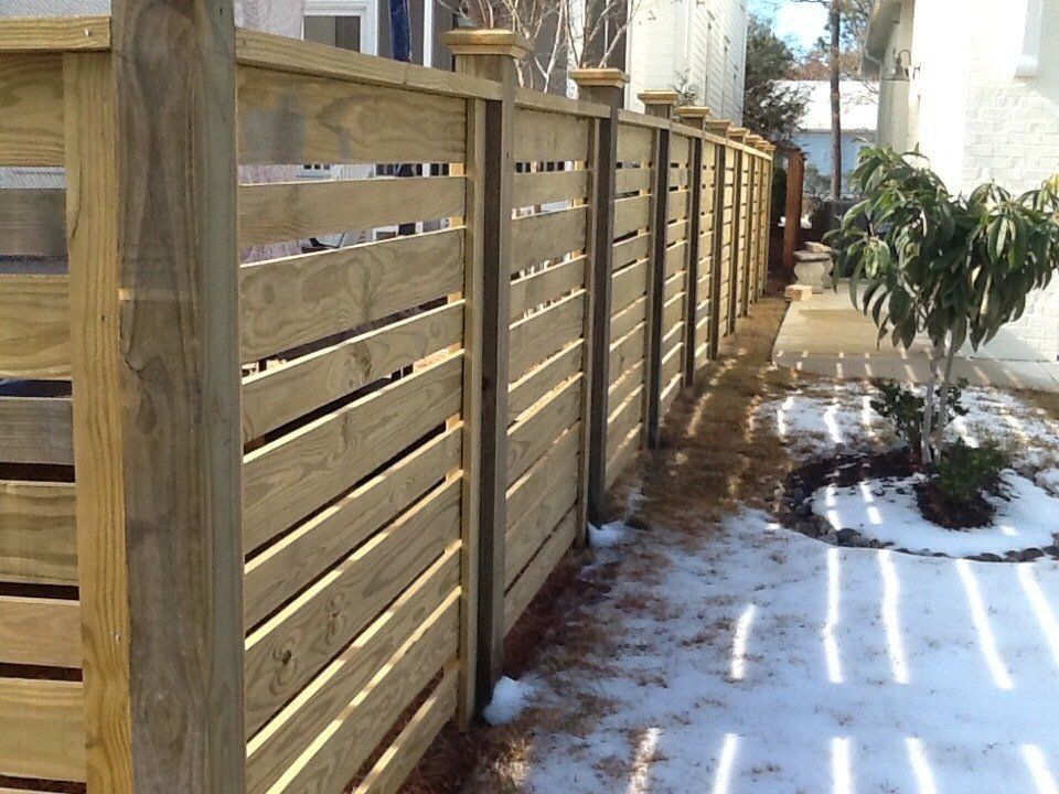 A wooden fence along a sidewalk with snow on the ground