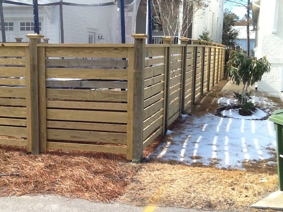 A wooden fence with a green trash can in front of it