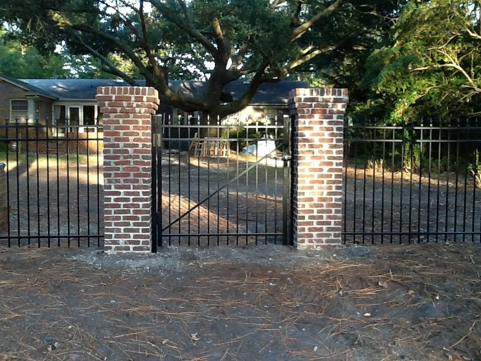 A metal fence with brick pillars in front of a house