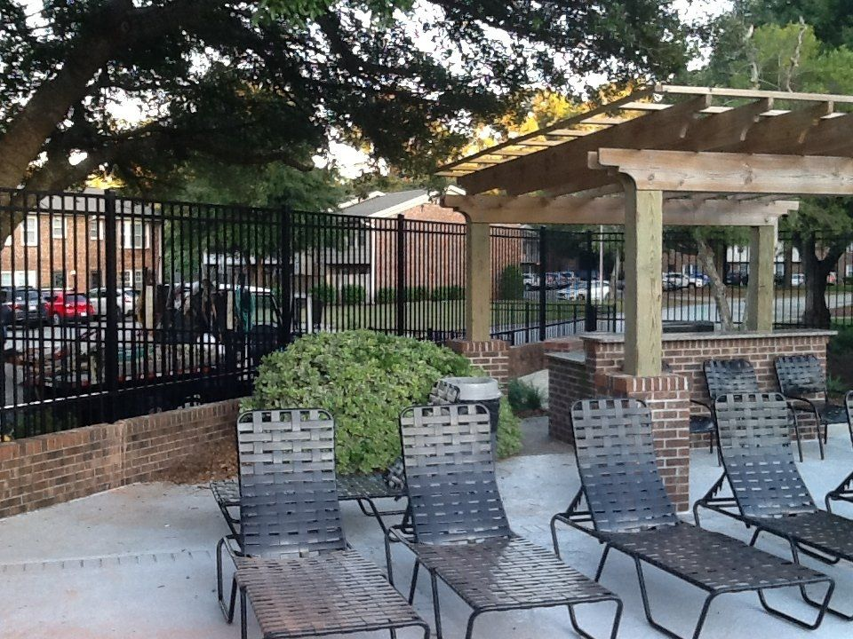 A row of lounge chairs under a pergola with a fence in the background