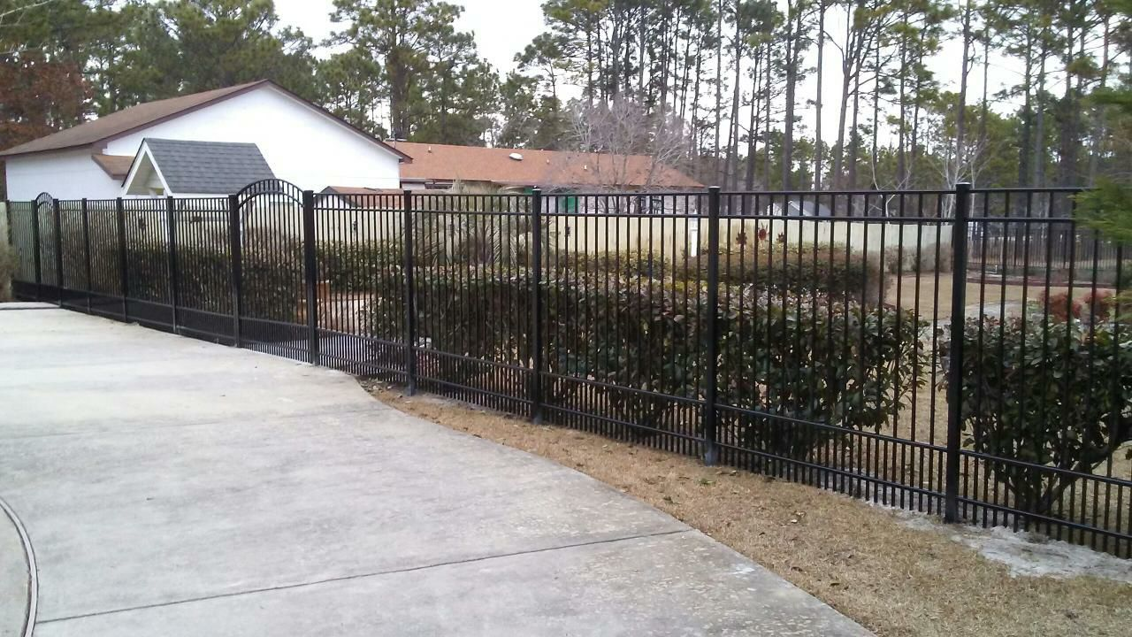 A black fence surrounds a driveway in front of a house