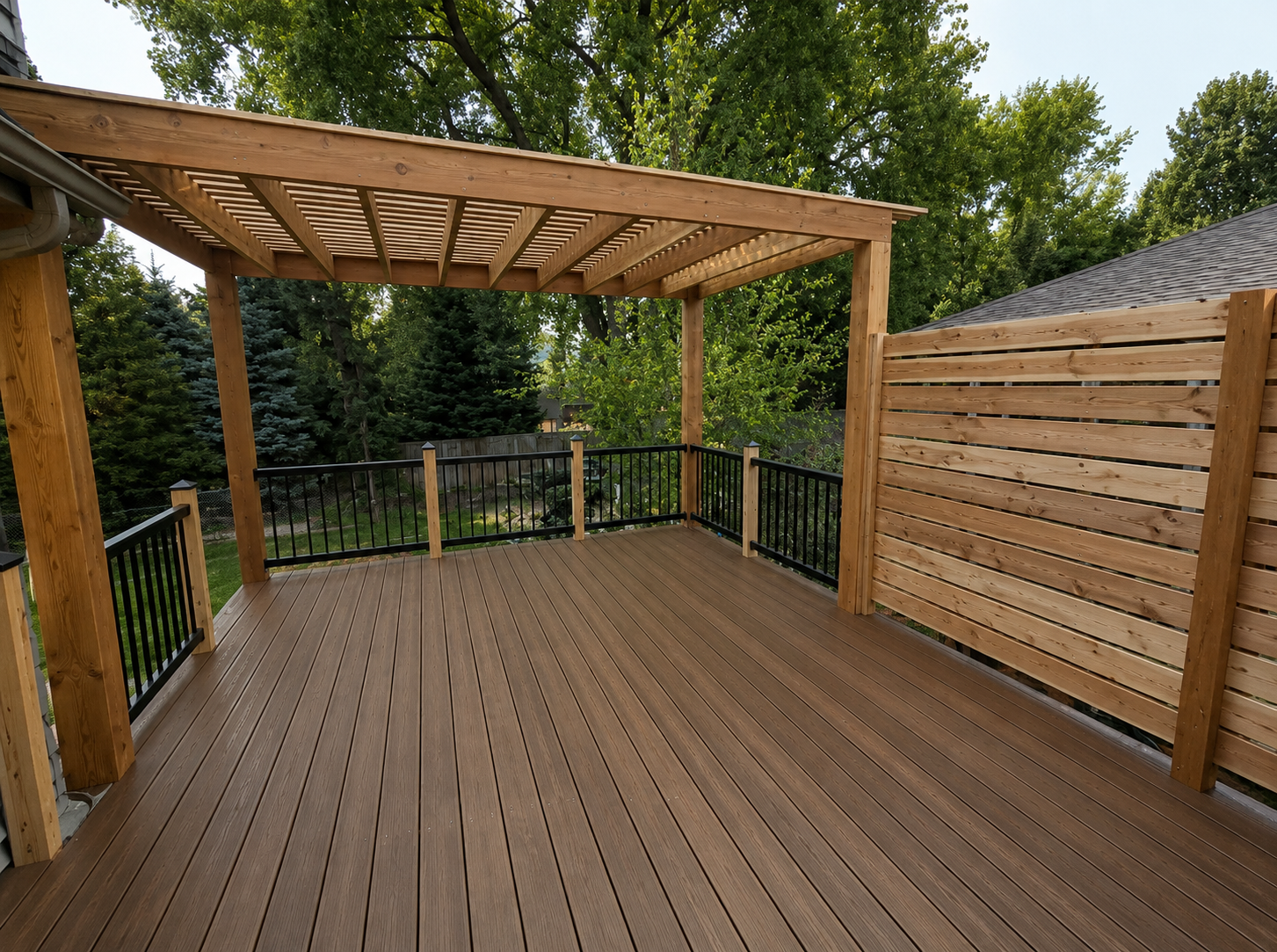 Wooden backyard deck with pergola and railing, bordered by a slatted fence and trees.