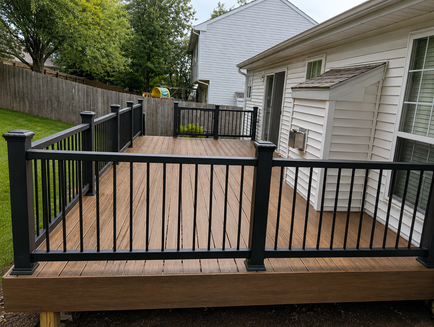 Wooden backyard deck with black railings beside a house and fenced yard