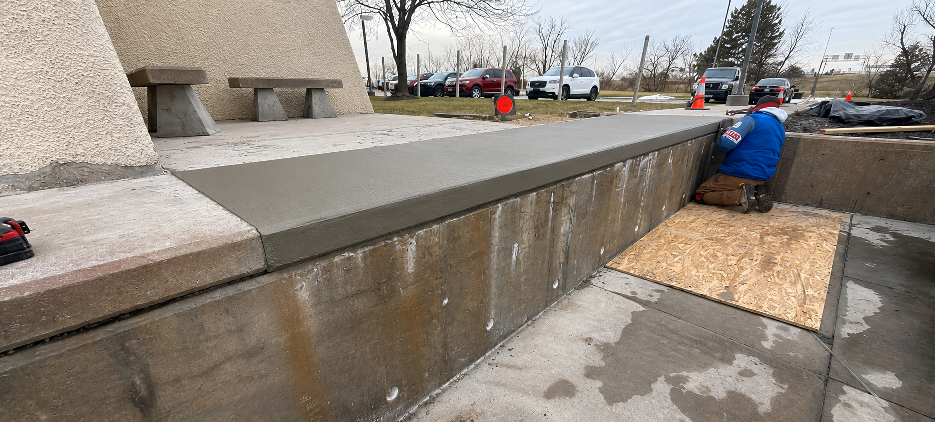 Worker applying material along a concrete wall beside a sidewalk on a rainy day