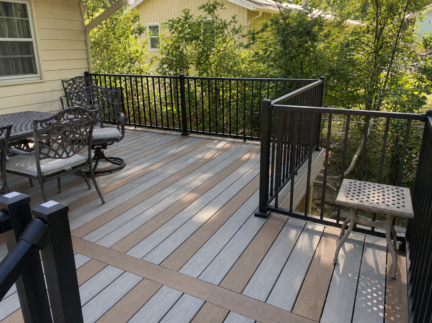 Patio deck with gray and tan flooring, black railings, and metal chairs beside a house