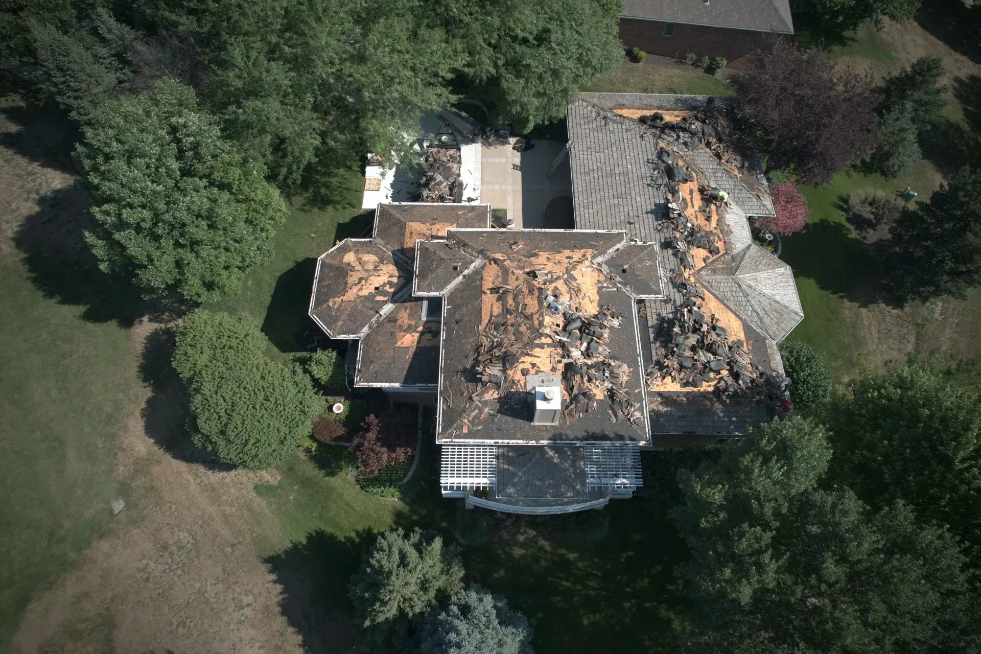 Aerial view of a residential house roof partially stripped of shingles, showing exposed wood decking and debris.