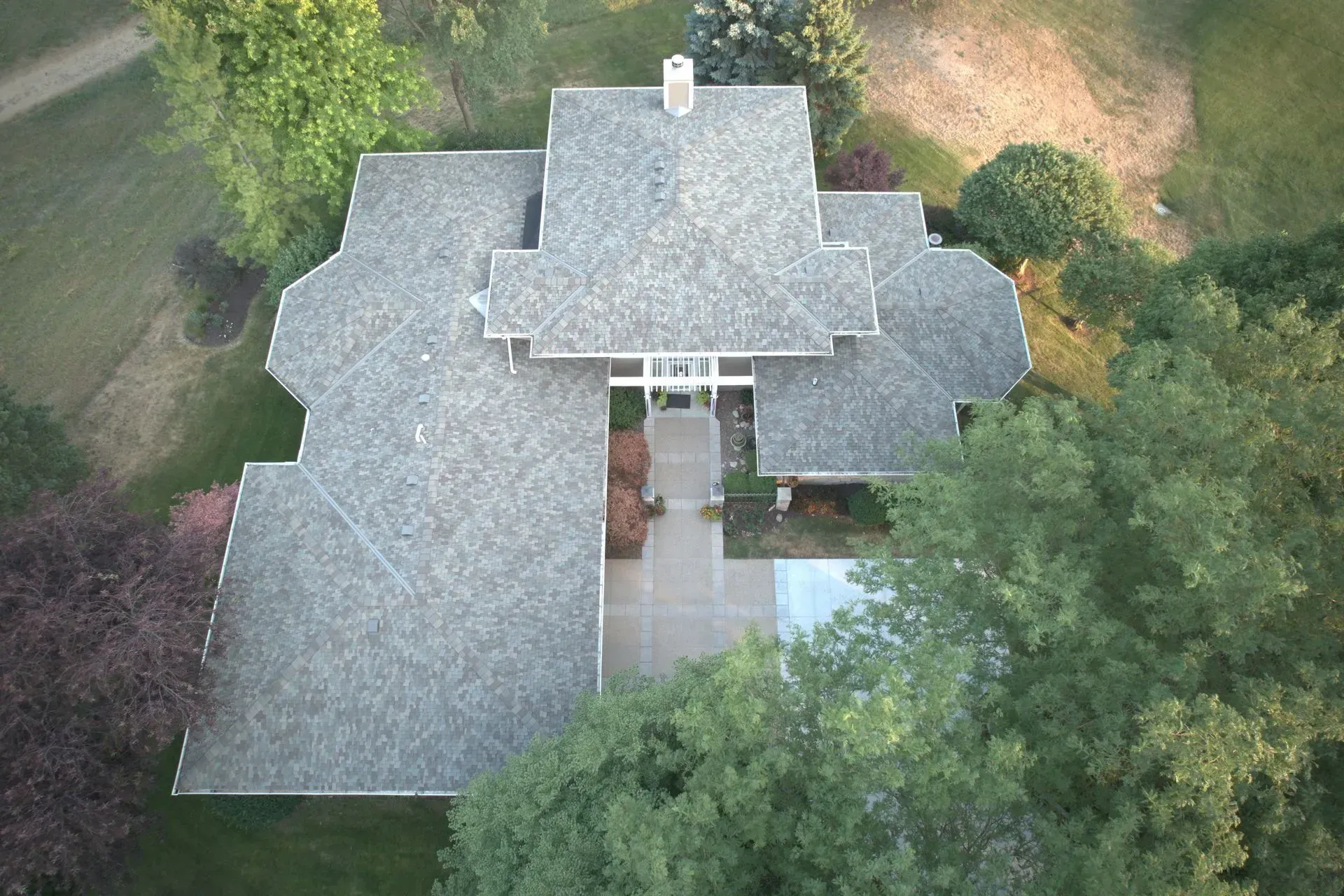 An aerial view of a house with a gray shingled roof, surrounded by green trees and a lawn.
