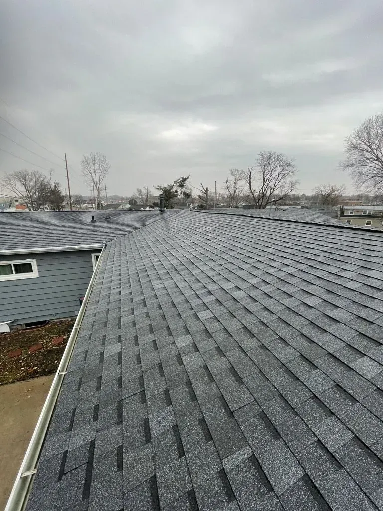 An angled view of a residential roof featuring newly installed, textured gray shingles under a cloudy sky.