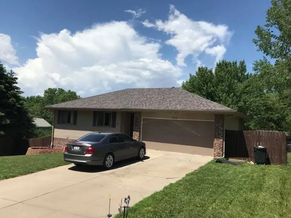 A single-story tan house with a dark roof and a two-car garage, with a gray car parked in the driveway.