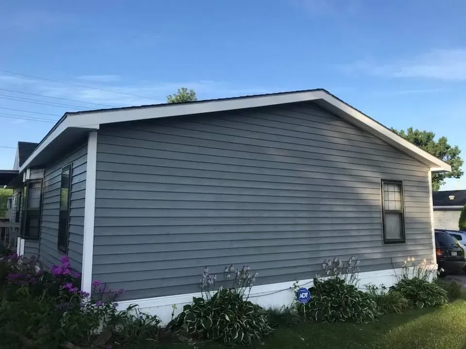 A single-story grey house with white trim and a gabled roof set against a clear blue sky.