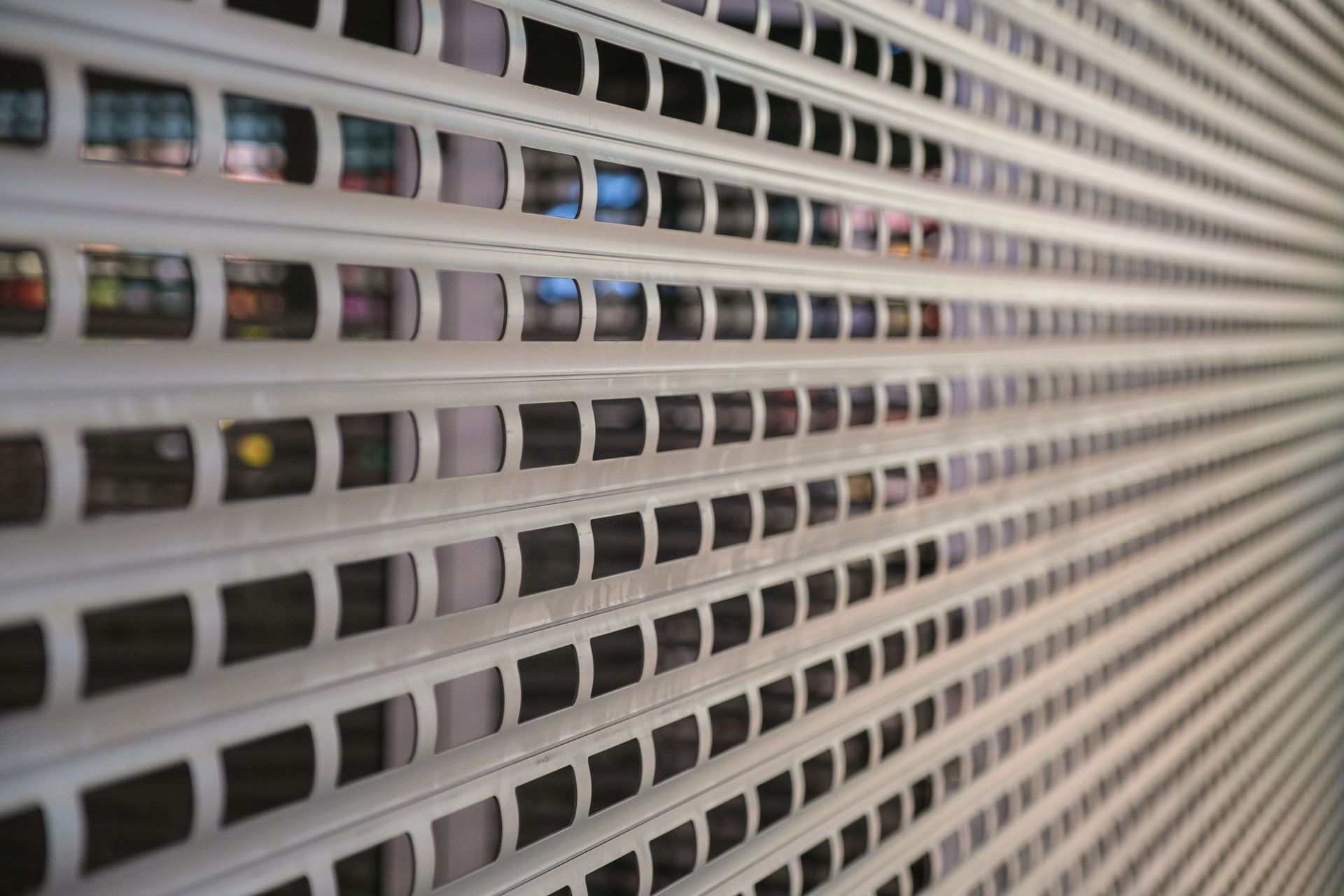 Row of small rectangular openings in a white perforated metal surface, viewed at an angle