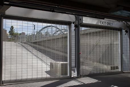 Gated exit with closed metal security fence and exit-only sign, opening to an outdoor walkway