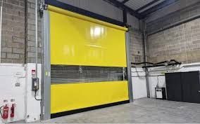 Yellow industrial roll-up door in a warehouse, with a metal inspection window and concrete walls.