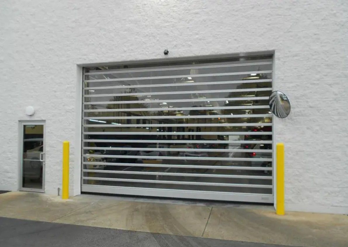 Closed metal garage door on white building, flanked by yellow bollards.
