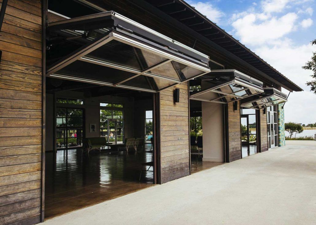 Covered outdoor walkway beside a brick building with open glass doors and a concrete path