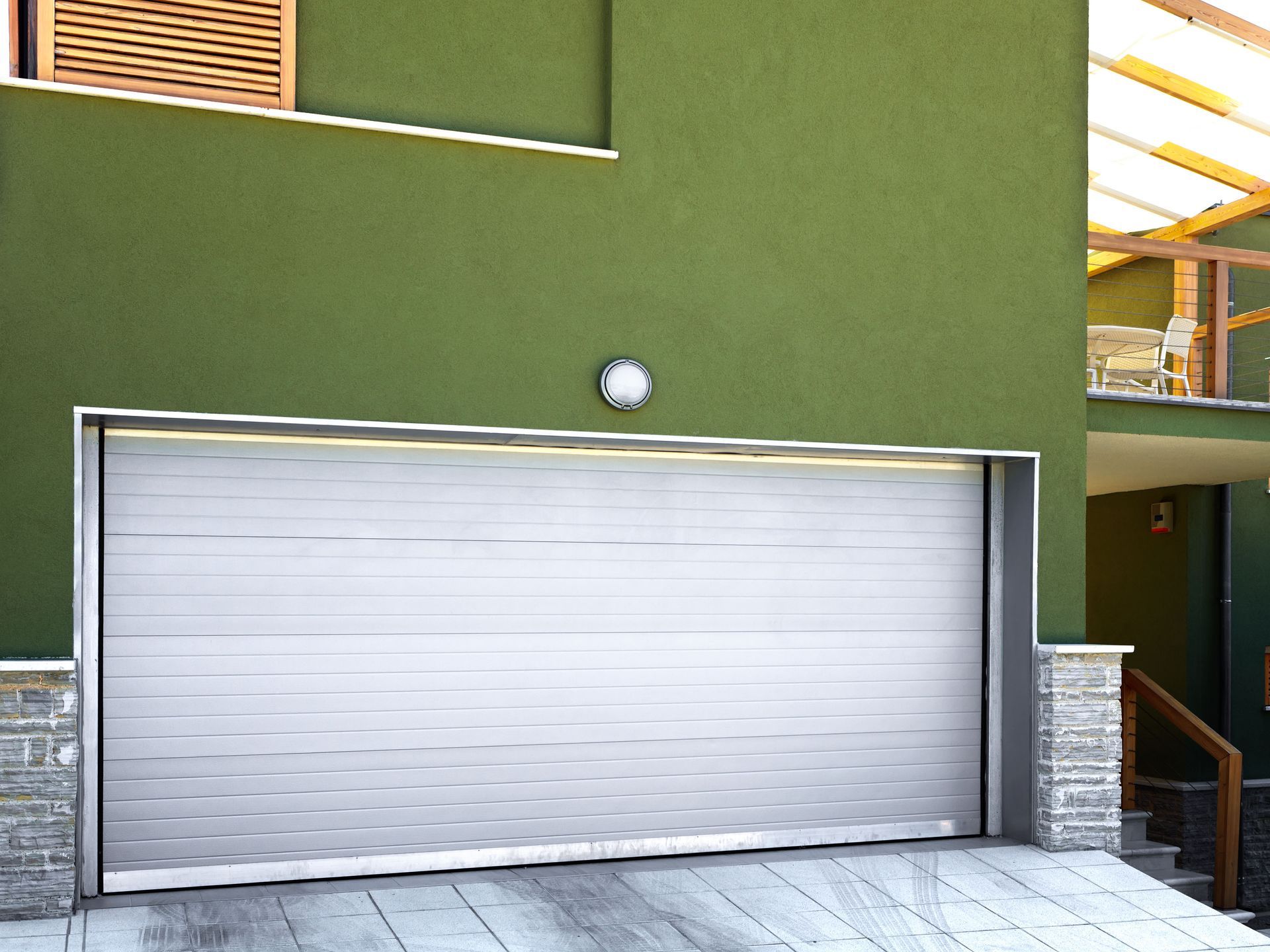 White garage door set in a green building with stone trim and exterior stairs.