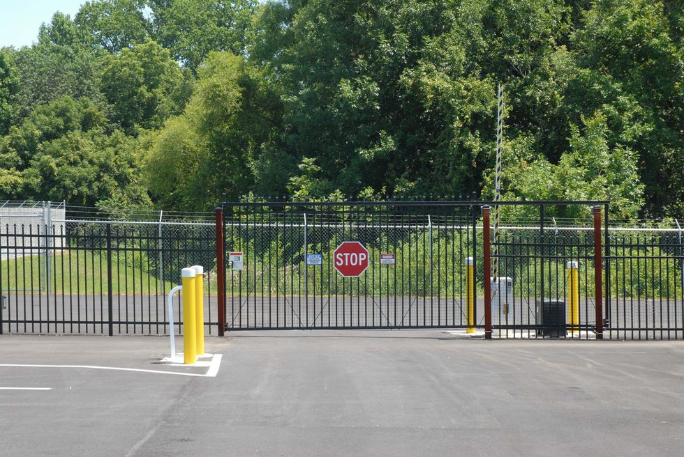 Gated driveway entrance with a stop sign, black metal fence, and trees beyond.