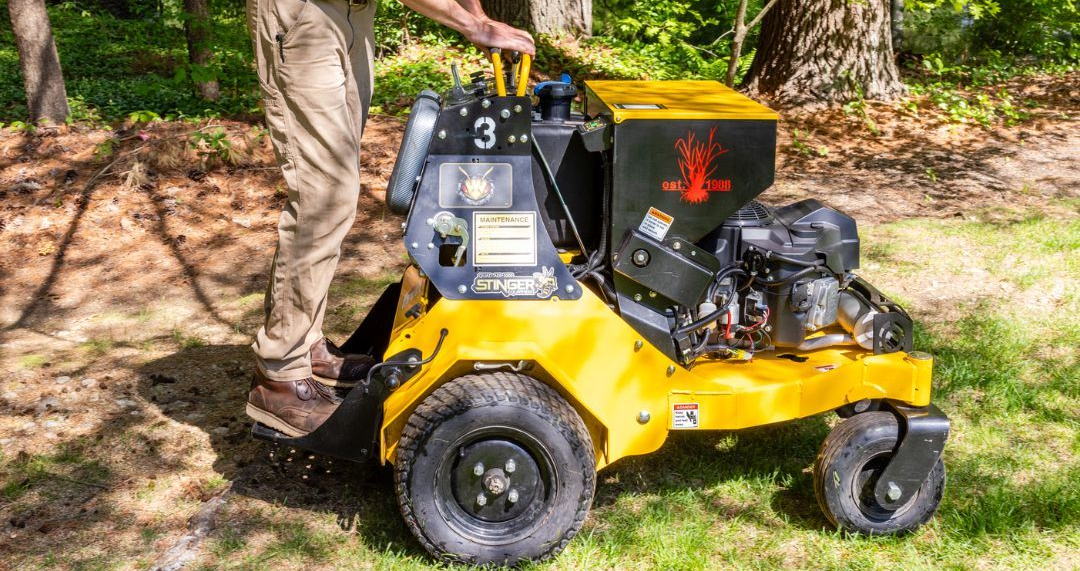 Person operating a yellow stump grinder on grassy ground.