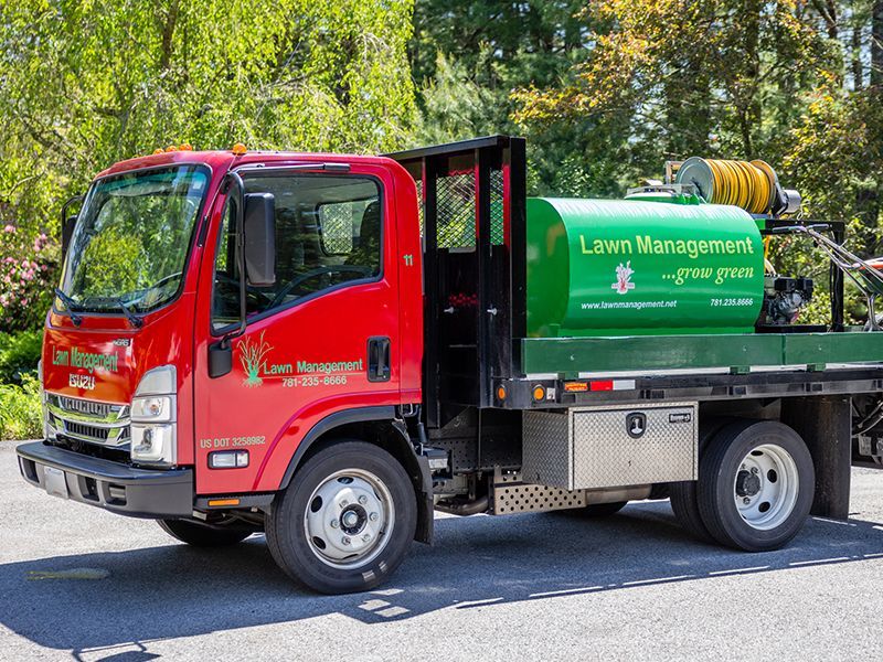 Man on red riding lawnmower cutting grass in a park, other lawnmower in the distance.