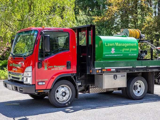 Man on red riding lawnmower cutting grass in a park, other lawnmower in the distance.