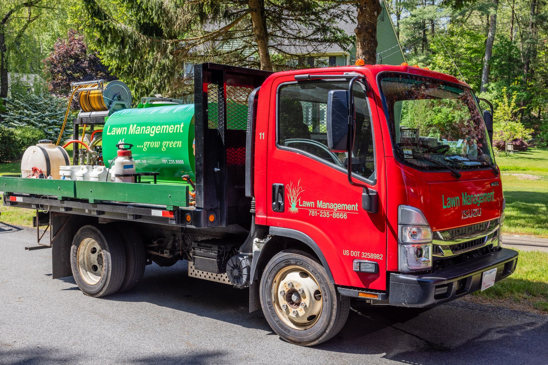 Red landscaping truck with green tank, parked on a road.